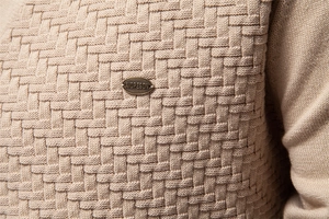 Macro detail of khaki knit sweater showing thick 3D crossover texture and metal brand tag