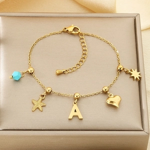 Detail of gold chain bracelet with sea star, letter A, and blue bead on silk fabric