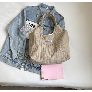 Beige Tragetasche mit Faltenstruktur neben Jeansjacke und Lifestyle-Accessoires