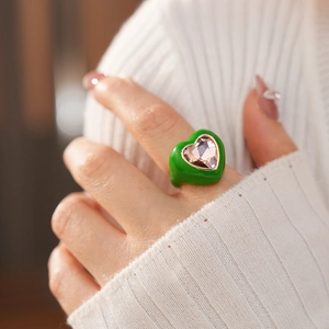 Close-up of a green enamel heart ring with a purple crystal on a finger