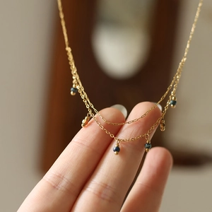 Hand holding double-layered 18K gold-plated necklace with vintage blue beads
