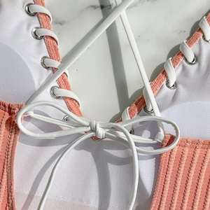 Detail of coral ribbed swimwear with white criss-cross laces and silver metal eyelets
