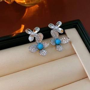 Detailed view of silver flower earrings with rhinestones, blue gems, and white pearls