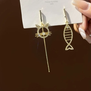 Detail of asymmetric gold tassel earrings with cat and fish bone crystal charms