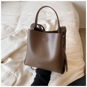 Detailed view of dark brown matte leather bucket bag resting on a white suit jacket