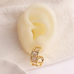 Dettaglio di un ear cuff dorato con zirconi a forma di cuore su un orecchio modello