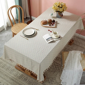Detail view of beige linen tablecloth with blue dots and tassels on a wooden dining table