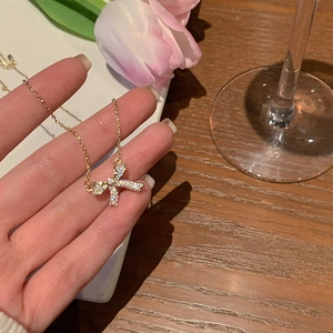 Elegant gold bow necklace with pavé zircon stones on a decorative floral background