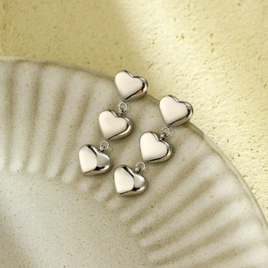 Detail view of triple heart dangle earrings in polished silver steel on ceramic plate