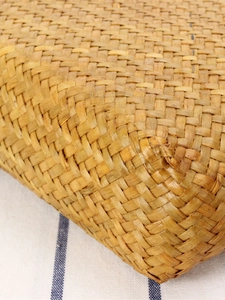 Handwoven straw shoulder bag with golden texture detail on a blue striped background