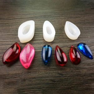 Silicone resin molds for DIY stone pendants in teardrop shapes on a dark wood background