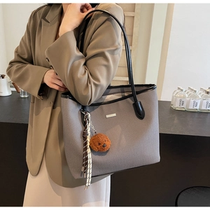 Detail of grey woven tote bag with leather trim and cute brown bear plush charm