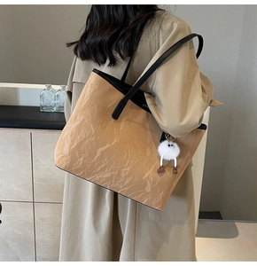 Dettaglio di una grande borsa tote kaki indossata a spalla con un ciondolo morbido decorativo