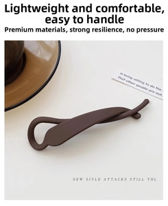 Close-up of matte dark brown hair clip with minimalist twisted arc design on beige surface