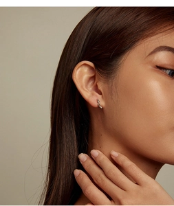 Close-up of model wearing silver snake hoop earrings with green zircon accents