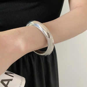 Gros plan d'un large bracelet argenté avec finition miroir polie au poignet d'un mannequin