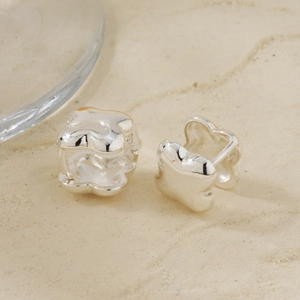 Detailed view of silver fluid star earrings on a textured minimalist sand background