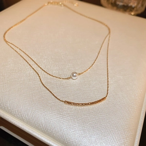 Detail of double-layer gold necklace with a white pearl and curved textured bar pendant