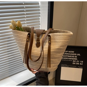 Detail view of woven straw tote bag featuring brown leather straps and vintage metal buckle