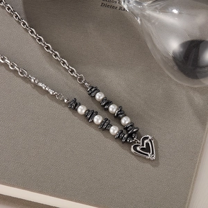 Detail of heart pendant necklace with black beads and white pearls on a grey background