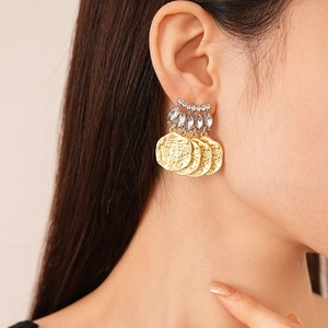 Détail de breloques en pièces d'or et accents de cristal sur une boucle d'oreille