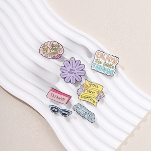 Set aus 9 bunten Emaille-Pins mit Motivationssprüchen auf weißem Wellen-Displayständer