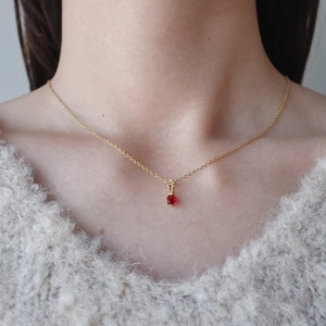 Primo piano di una collana placcata oro con ciondolo tondo in pietra portafortuna rossa su modella