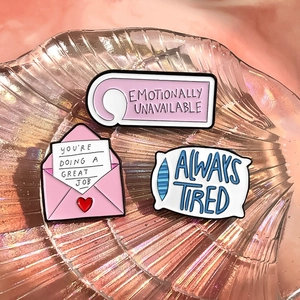 Macro shot of three colorful enamel pins with motivational slogans on a shell tray