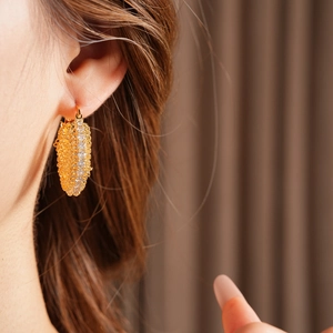 Close-up of a gold-plated geometric link earring with white zircon inlay worn by a model