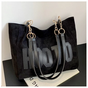 Detail of black tote bag featuring matte texture and gold chain shoulder strap