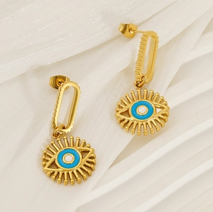 Detailed close-up of gold evil eye drop earrings with blue enamel on white fabric
