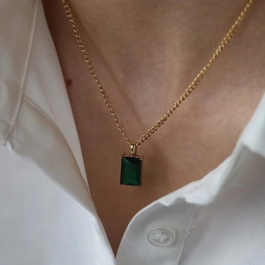 Golden necklace with emerald rectangle zircon pendant on model wearing white shirt