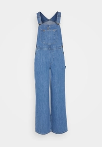 Detail of light blue denim overalls showing front pocket and metal strap buckles