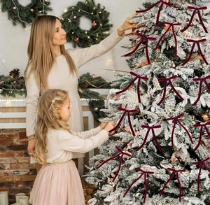 Family decorating Christmas tree with deep red velvet bows in a warm home setting