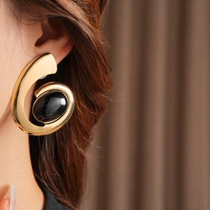 Close-up of a large gold spiral earring with a black oval gemstone worn by a model