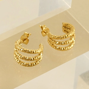 Three-layer golden C-shaped hoop earrings with hammered texture finish on acrylic stand