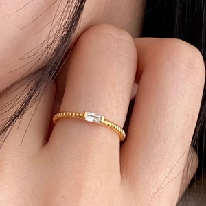 Dettaglio di un anello dorato a treccia con una gemma trasparente taglio baguette