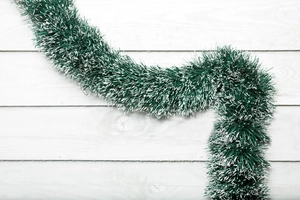 Macro shot of 2m dark green Christmas tinsel garland with white snow tips on wood