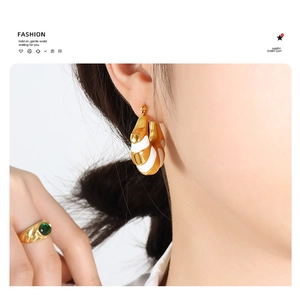 Model wearing gold and white enamel C-shape earrings with a green emerald wide band ring