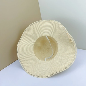 Detail of cream straw hat featuring intricate crochet lace edge and white elastic wind cord