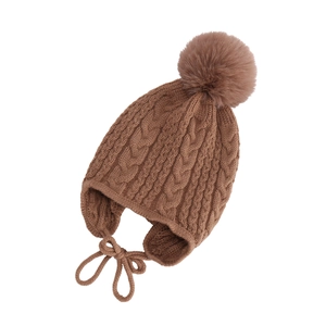 Detail of baby knitted hat showing brown cable knit pattern and fuzzy pom pom trim