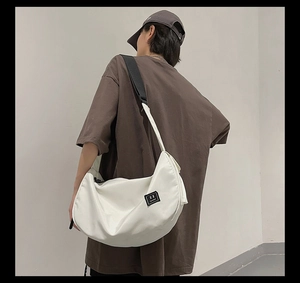 Close-up of white crescent crossbody bag with black adjustable strap and square logo detail