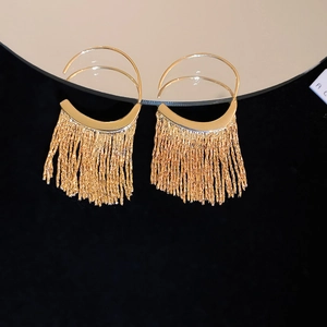 Gros plan de boucles d'oreilles à pompons dorés avec demi-cercles polis reflétés sur un miroir