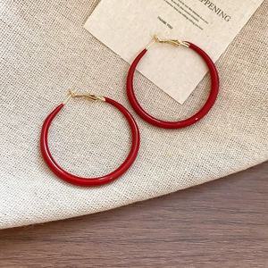 Macro shot of minimalist deep red hoop earrings with polished finish and gold hooks