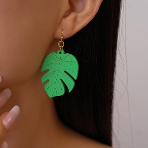 Detail of tropical monstera leaf wooden earring with green paint and gold hook on model