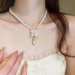 Détail d'un collier de perles avec des roses roses et un pendentif perle en goutte d'eau