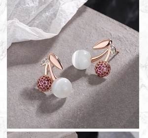 Detail view of cherry earrings with rose gold base, opal stones and red zircon leaves
