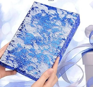 Close-up of hands holding a blue gift box with gold foil mesh texture and ribbon detail