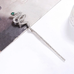 Detailed macro shot of silver metal snake hair pin with green gemstone eye on white background