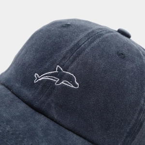 Detailaufnahme der weißen Delfinstickerei auf der dunkelblauen Baseballkappe aus Baumwolle